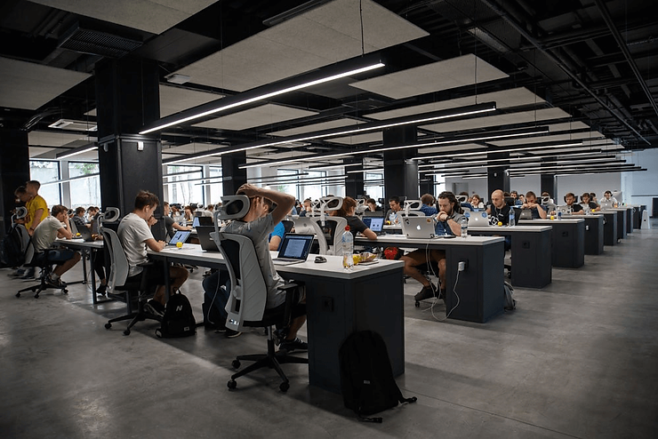 A wide photo of a large open-plan office full of people working at long desks.