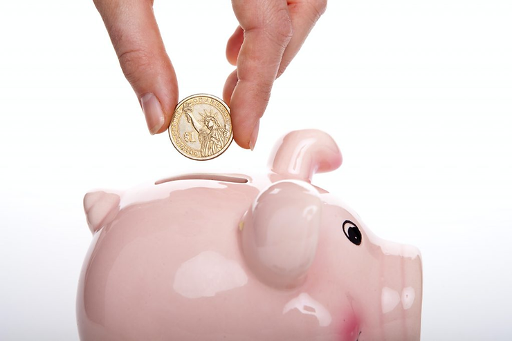 A hand dropping a gold dollar coin into a pink piggy bank.