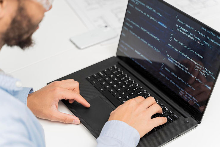 Person typing on a laptop with code on screen, in a bright office setting. The mood is focused, with a light blue shirt and black laptop.