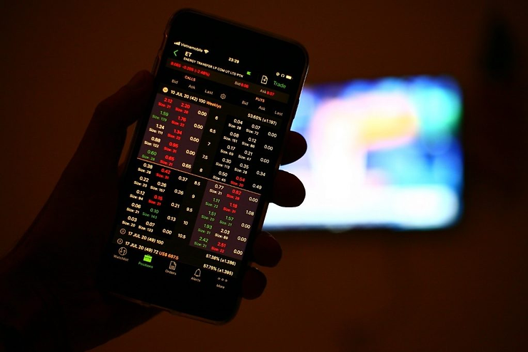 Hand holding a smartphone displaying a stock trading app with red and green numbers, against a blurred, colorful background.