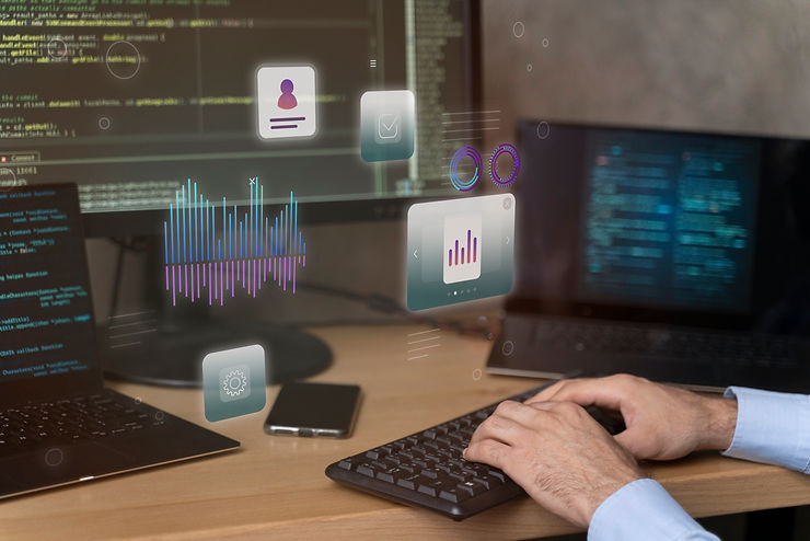Hands typing on a keyboard at a desk with multiple screens showing code. Holographic graphs and icons float above. Modern tech vibe.