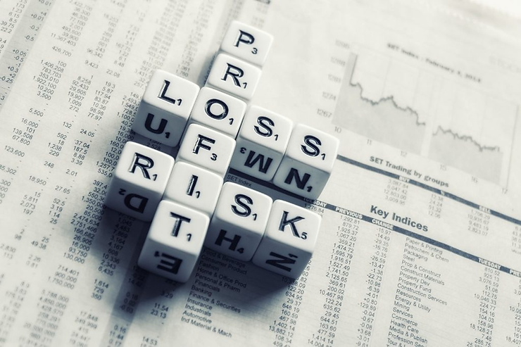 Letter dice spelling "PROFIT" and "LOSS" on financial newspaper with stock chart blurred in background. Neutral mood.